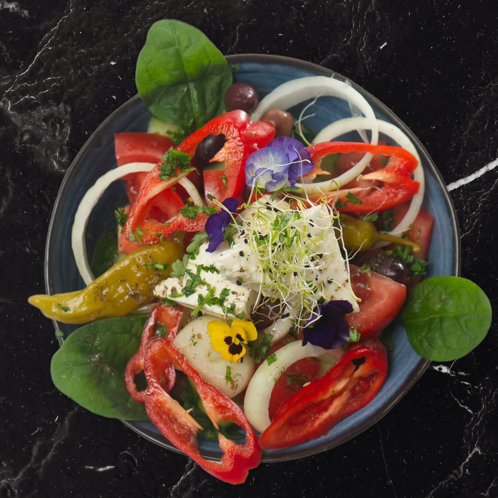 Griekse boerensalade met tomaat, komkommer, paprika, ui, olijven en een blok feta met eetbare viooltjes.